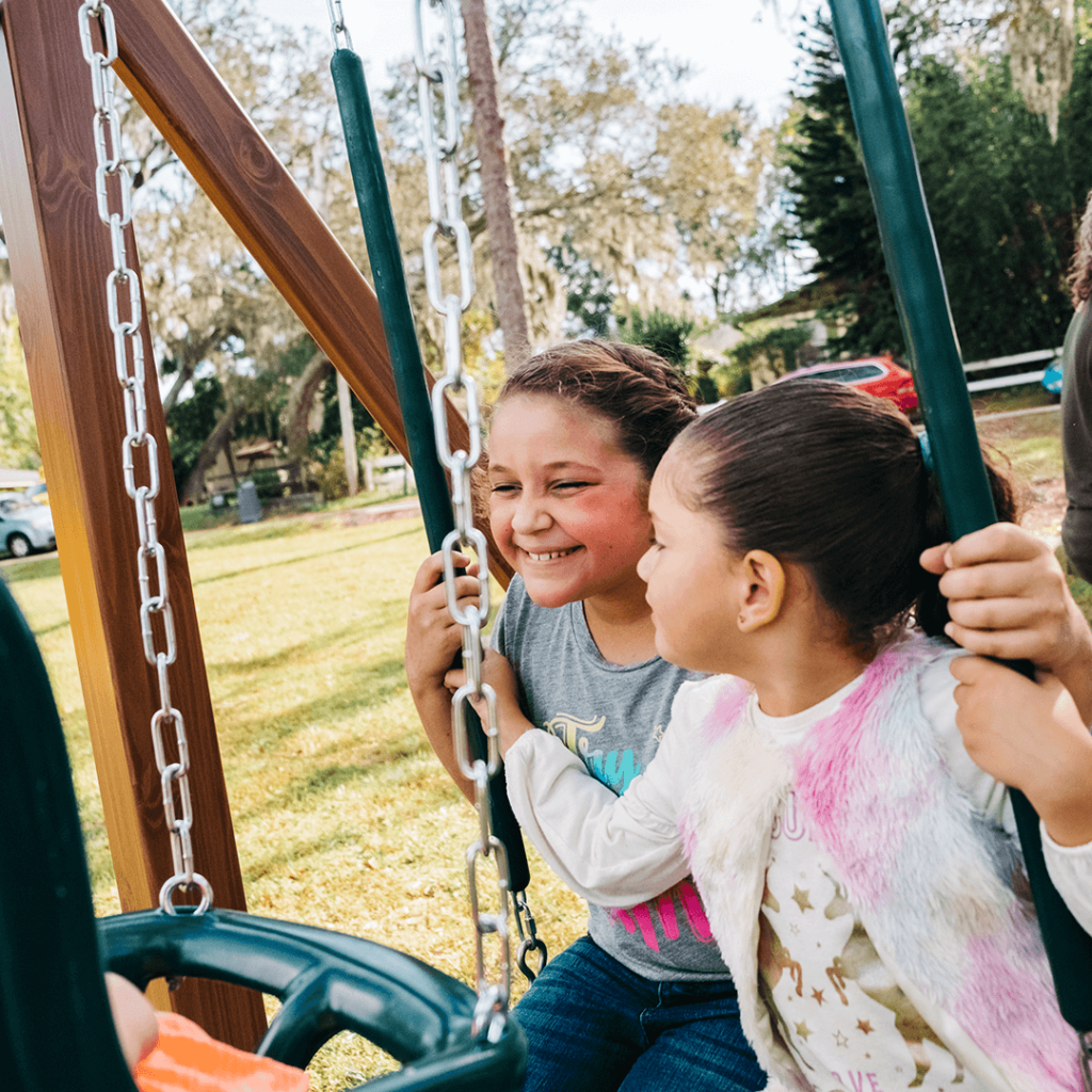 2 girls swinging on a backyard playset smiling